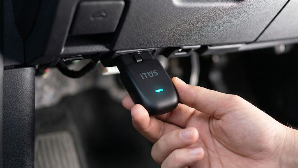 A close-up of the Datakrew ITUS Max OBD-II sensor being plugged into a car dashboard port for real-time battery monitoring.